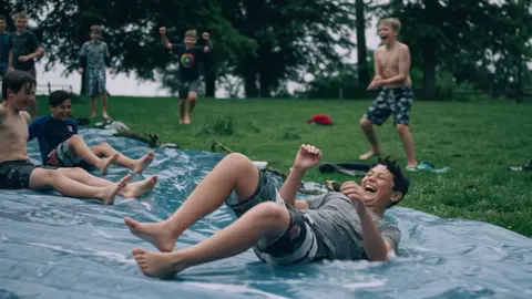 Gemini Omni Flash clip: teenage boys sliding down a wet plastic tarp on a lawn