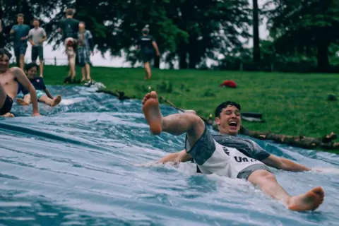Kling 3.0 clip: teenage boys sliding down a wet plastic tarp on a lawn