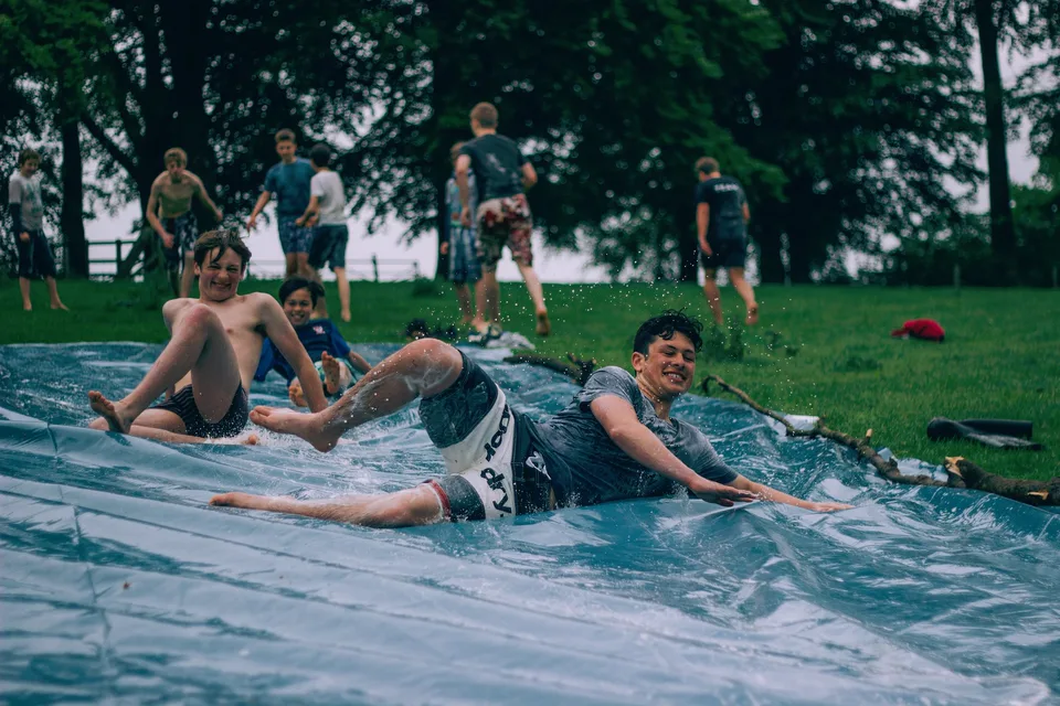 Teenage boys sliding down a wet plastic tarp on a lawn