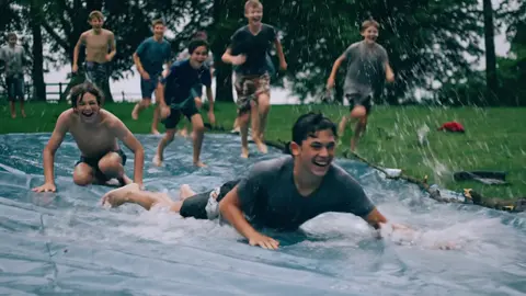 Veo 3.1 Fast clip: teenage boys sliding down a wet plastic tarp on a lawn