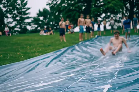 Wan 3.0 clip: teenage boys sliding down a wet plastic tarp on a lawn